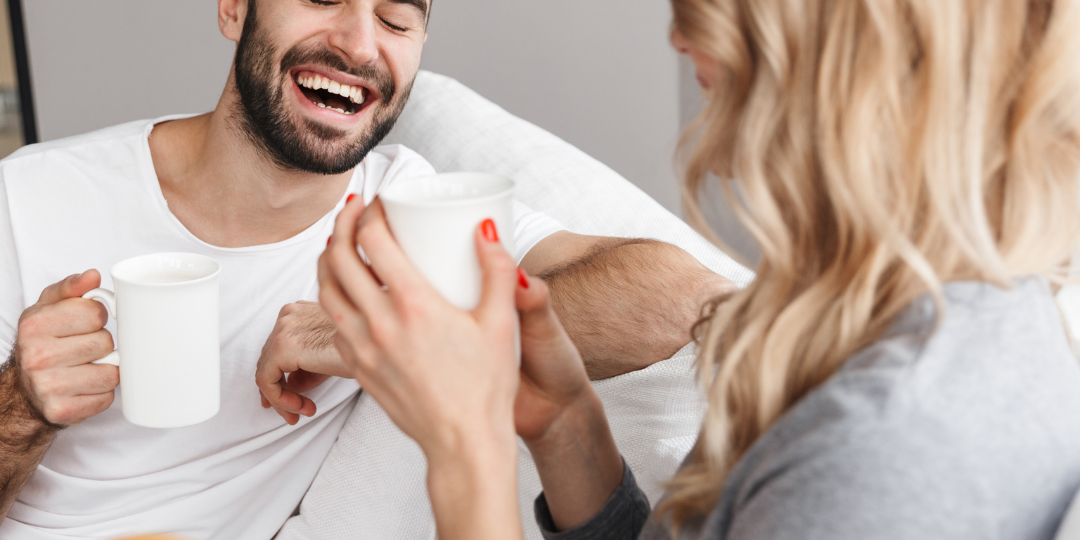 couple laughing on the couch holding coffee mugs