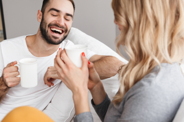 couple laughing on the couch holding coffee mugs