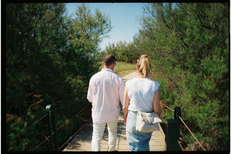 pexels-photo-23413620-23413620 Back view of a couple walking hand in hand on a wooden bridge surrounded by greenery.