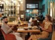 Couple enjoying a meal and conversation at a stylish restaurant, using smartphones and wine glasses present.