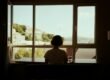 A woman sitting at a table, looking out a window in soft daylight.