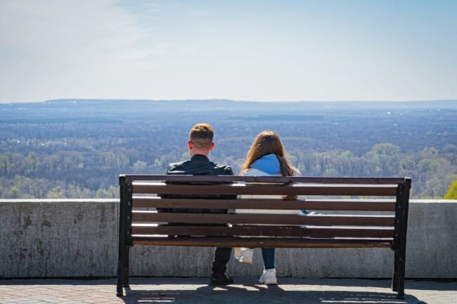 A couple sitting on a bench, a quiet distance between them.