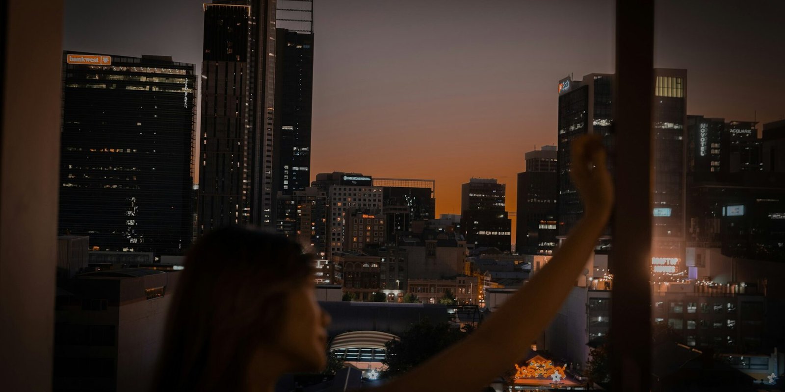 A person looking out at the city lights at night, alone.