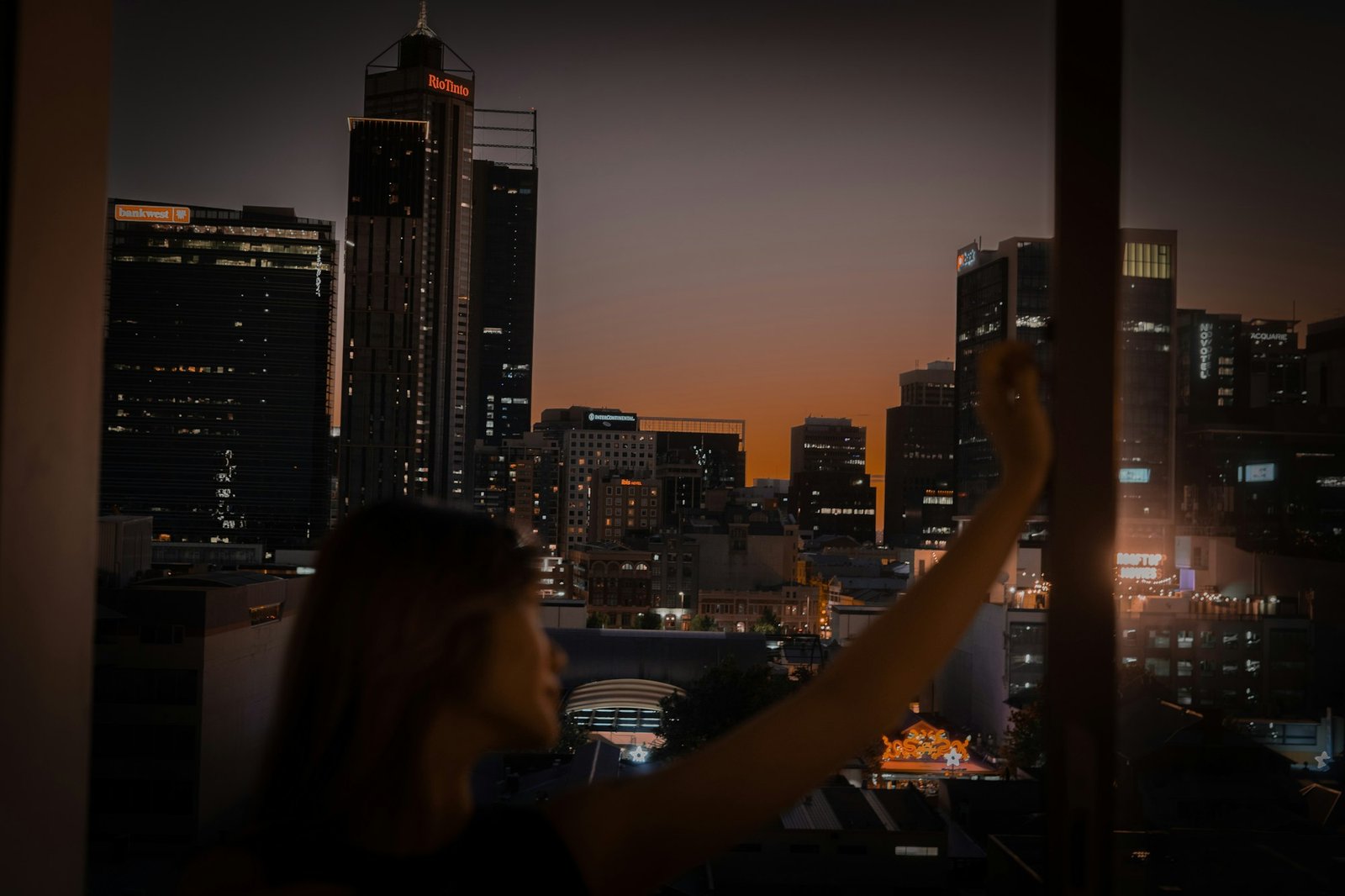 A person looking out at the city lights at night, alone.