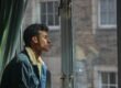 A man looking out a window, withdrawn and pensive.