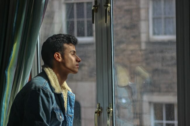 A man looking out a window, withdrawn and pensive.