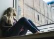 A woman sitting by a window, gazing out at the sky.