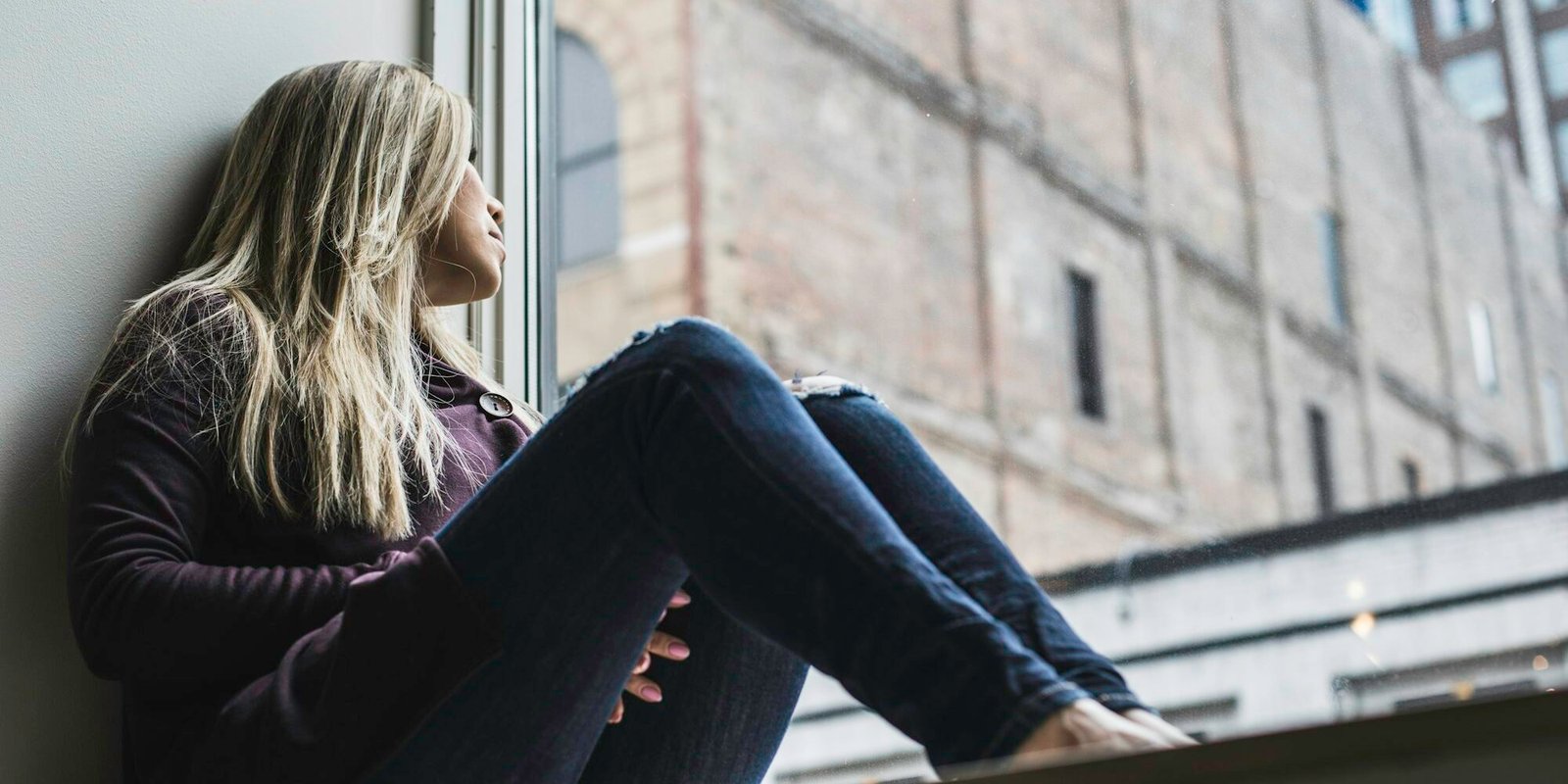 A woman sitting by a window, gazing out at the sky.