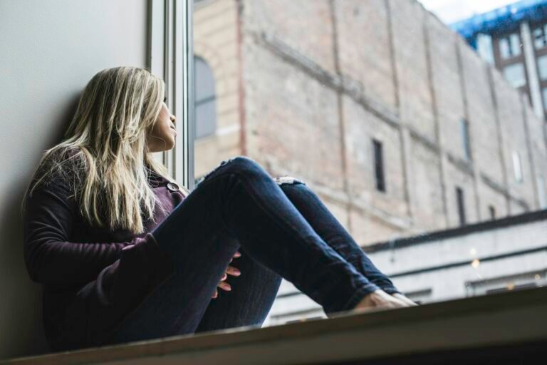 A woman sitting by a window, gazing out at the sky.