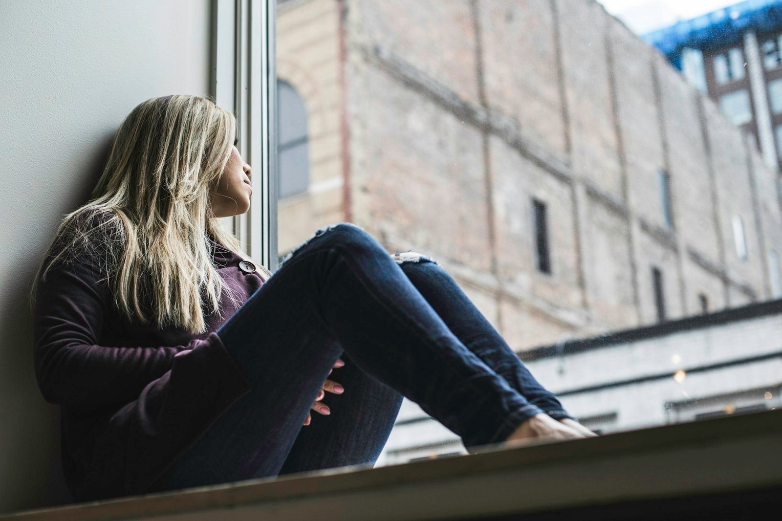 A woman sitting by a window, gazing out at the sky.