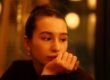 A woman seated in soft indoor light, thoughtfully working something out.