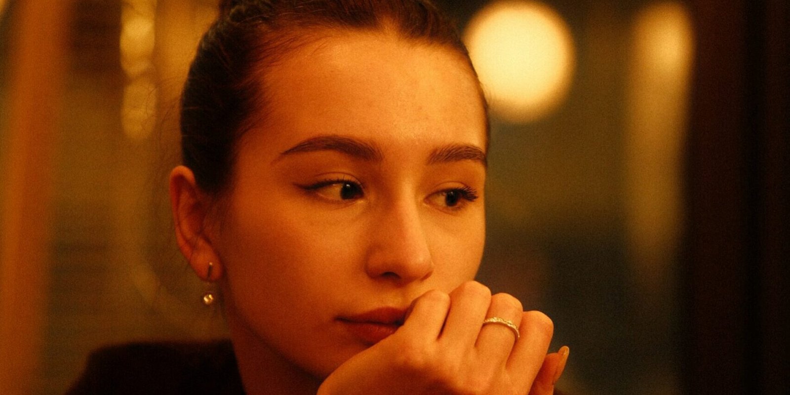A woman seated in soft indoor light, thoughtfully working something out.