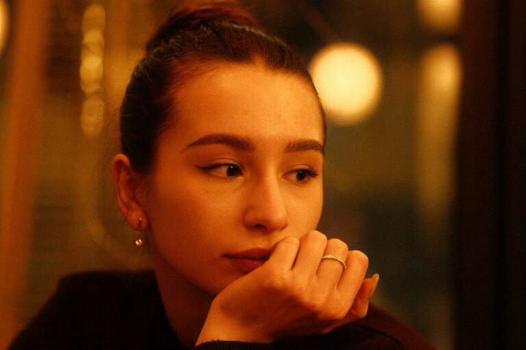 A woman seated in soft indoor light, thoughtfully working something out.