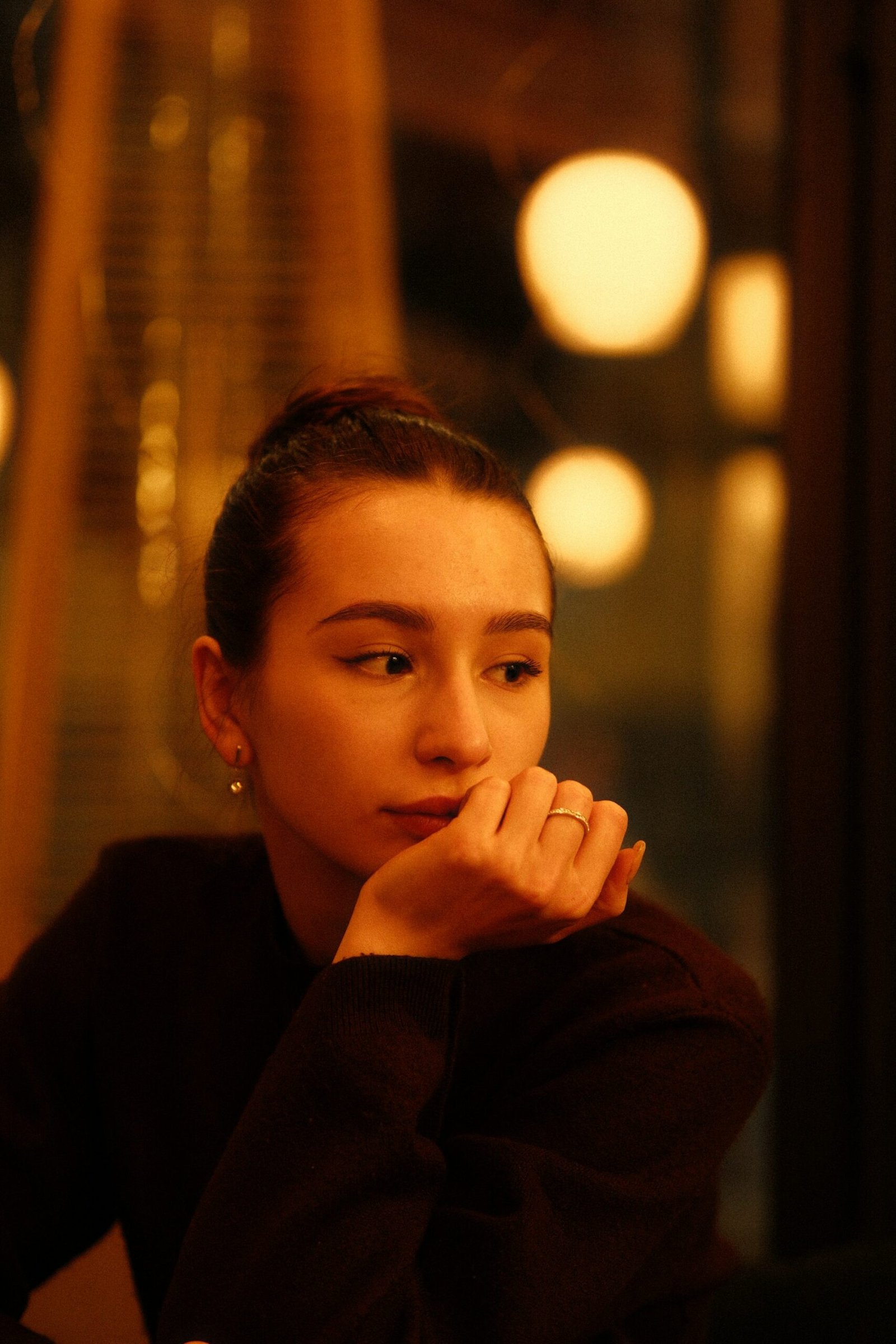 A woman seated in soft indoor light, thoughtfully working something out.