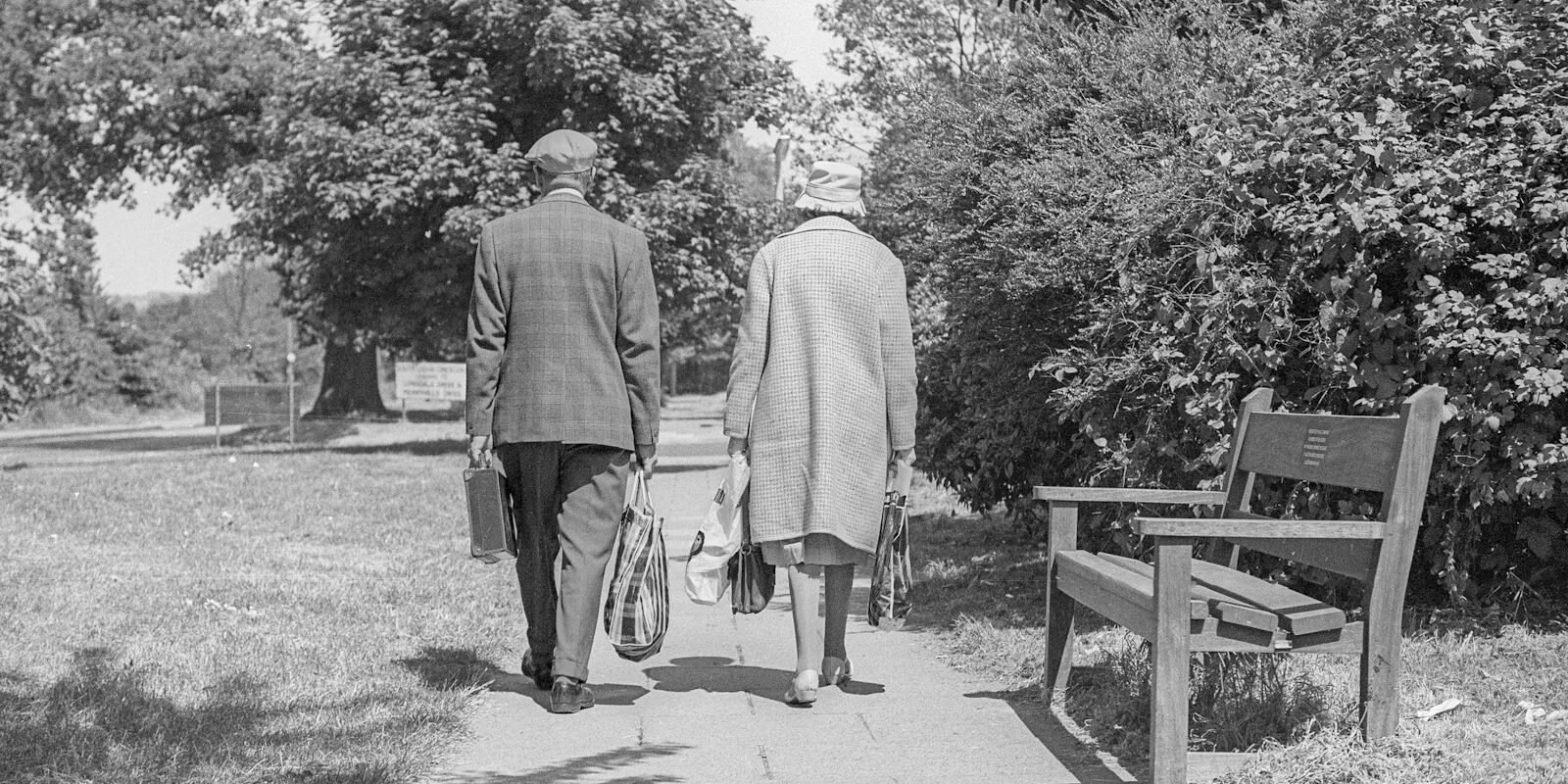 An older couple walking together on a tree-lined path.