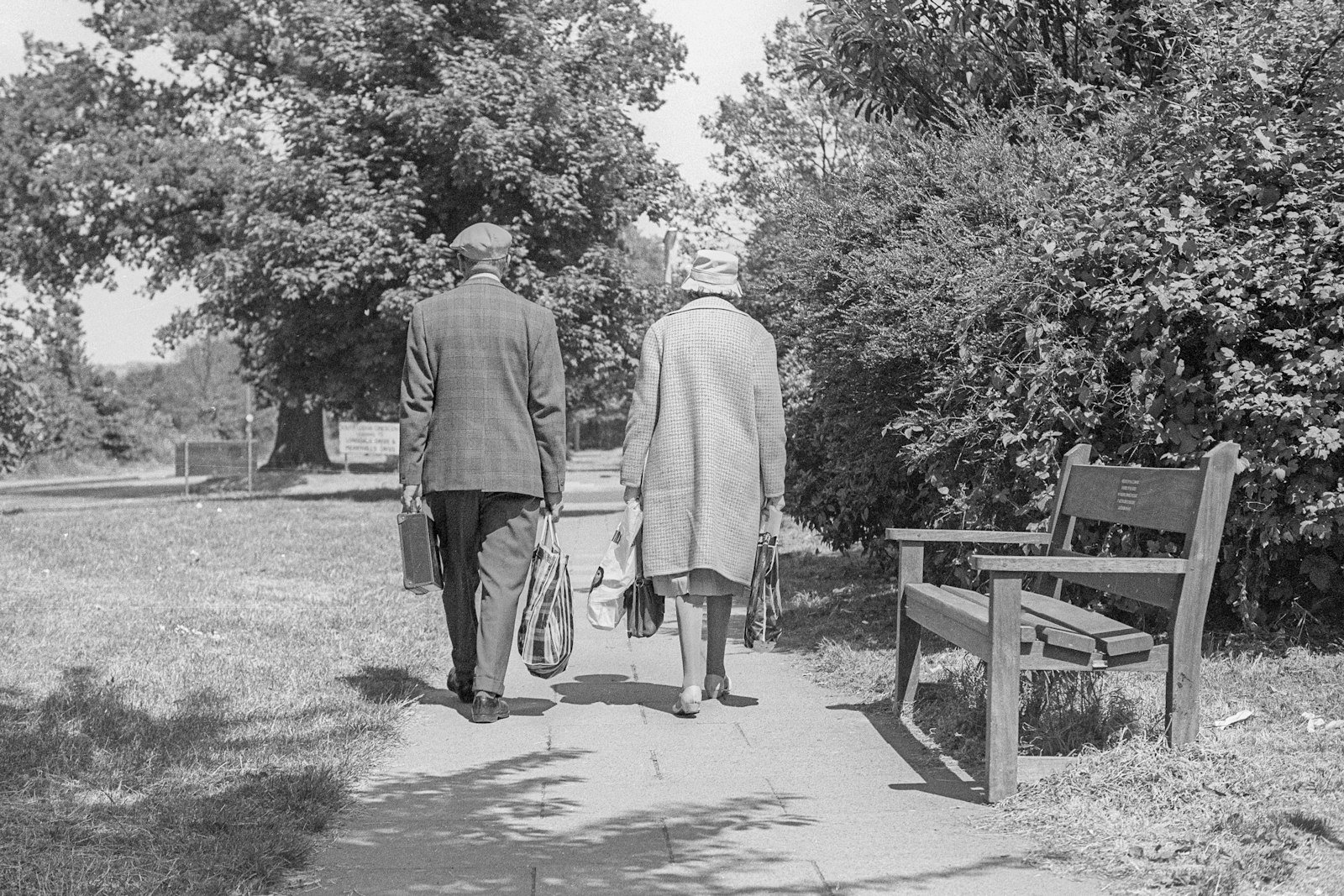 An older couple walking together on a tree-lined path.