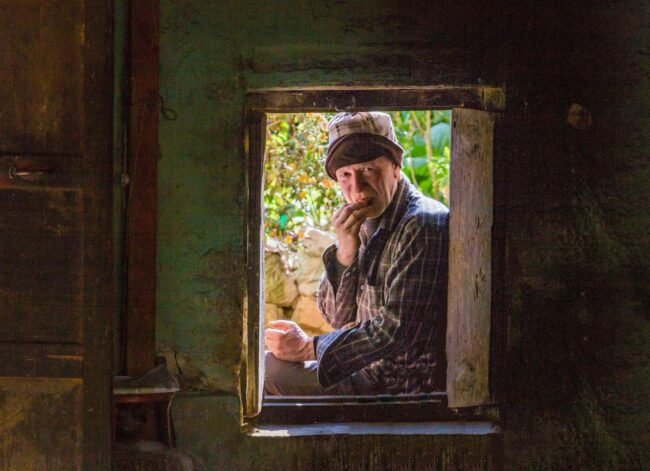 An older man by a window, quiet and thoughtful.