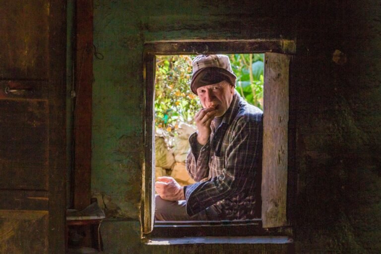 An older man by a window, quiet and thoughtful.