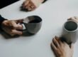 Two people across a small cafe table, mid-conversation over coffee.