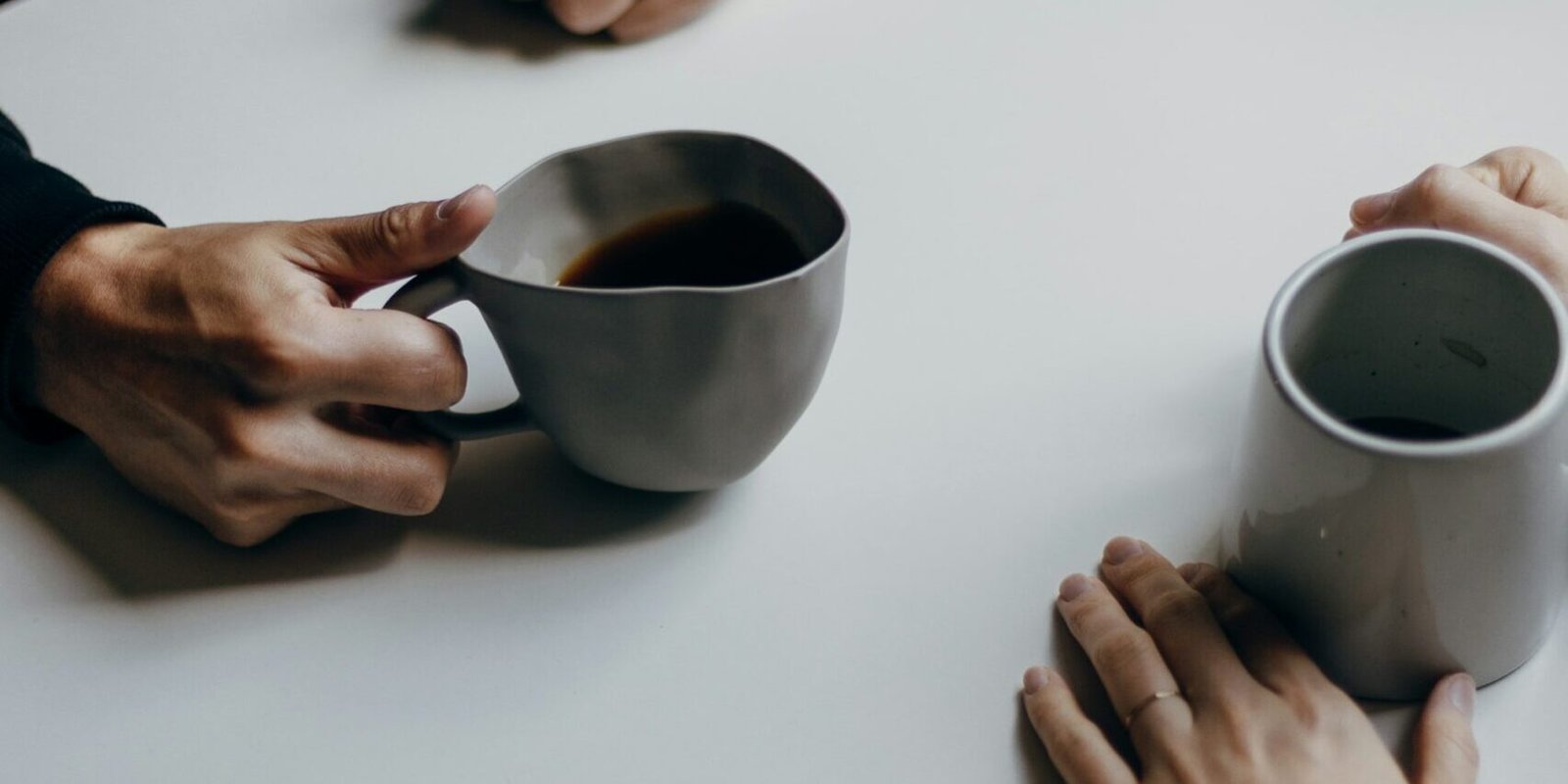 Two people across a small cafe table, mid-conversation over coffee.