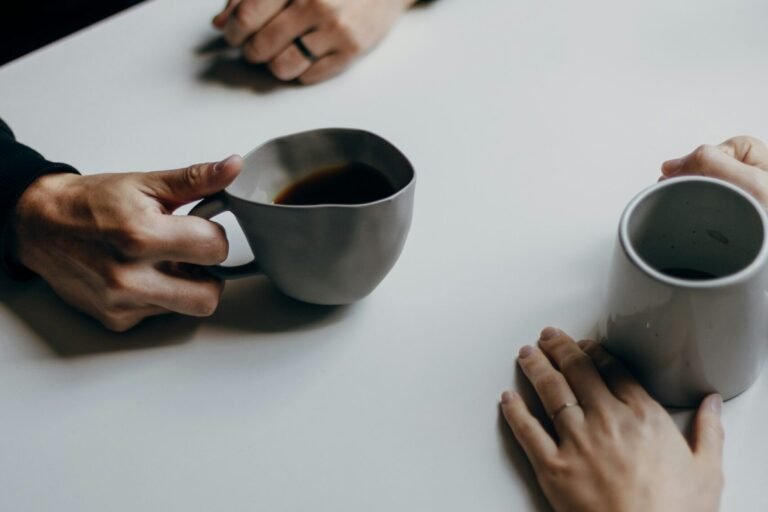 Two people across a small cafe table, mid-conversation over coffee.